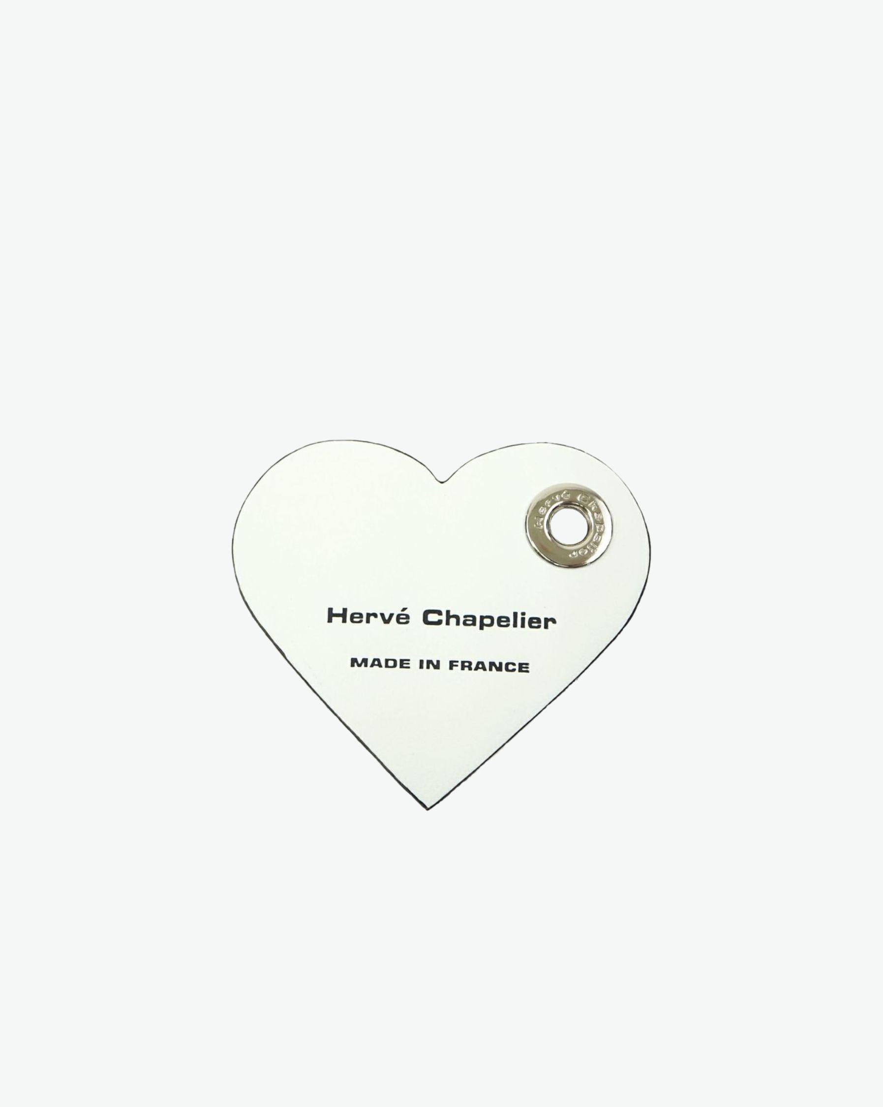 Packshot of a 122L flat charm in the shape of a heart with the Hervé Chapelier logo. The charm is made of leather with a eyelet in the middle in a XXS size. Charme en forme de coeur en cuir dans une taille XXS
