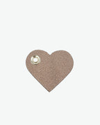 Packshot of a 122L flat charm in the shape of a heart with the Hervé Chapelier logo. The charm is made of leather with a eyelet in the middle in a XXS size. Charme en forme de coeur en cuir dans une taille XXS
