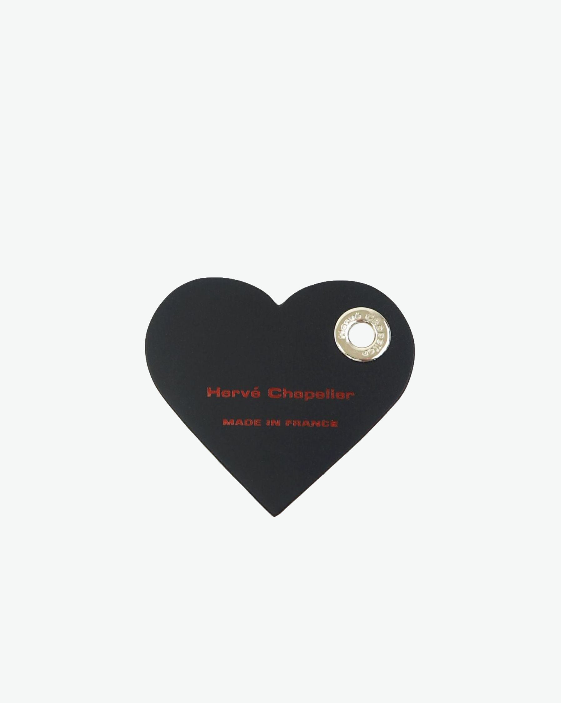 Packshot of a 122L flat charm in the shape of a heart with the Hervé Chapelier logo. The charm is made of leather with a eyelet in the middle in a XXS size. Charme en forme de coeur en cuir dans une taille XXS