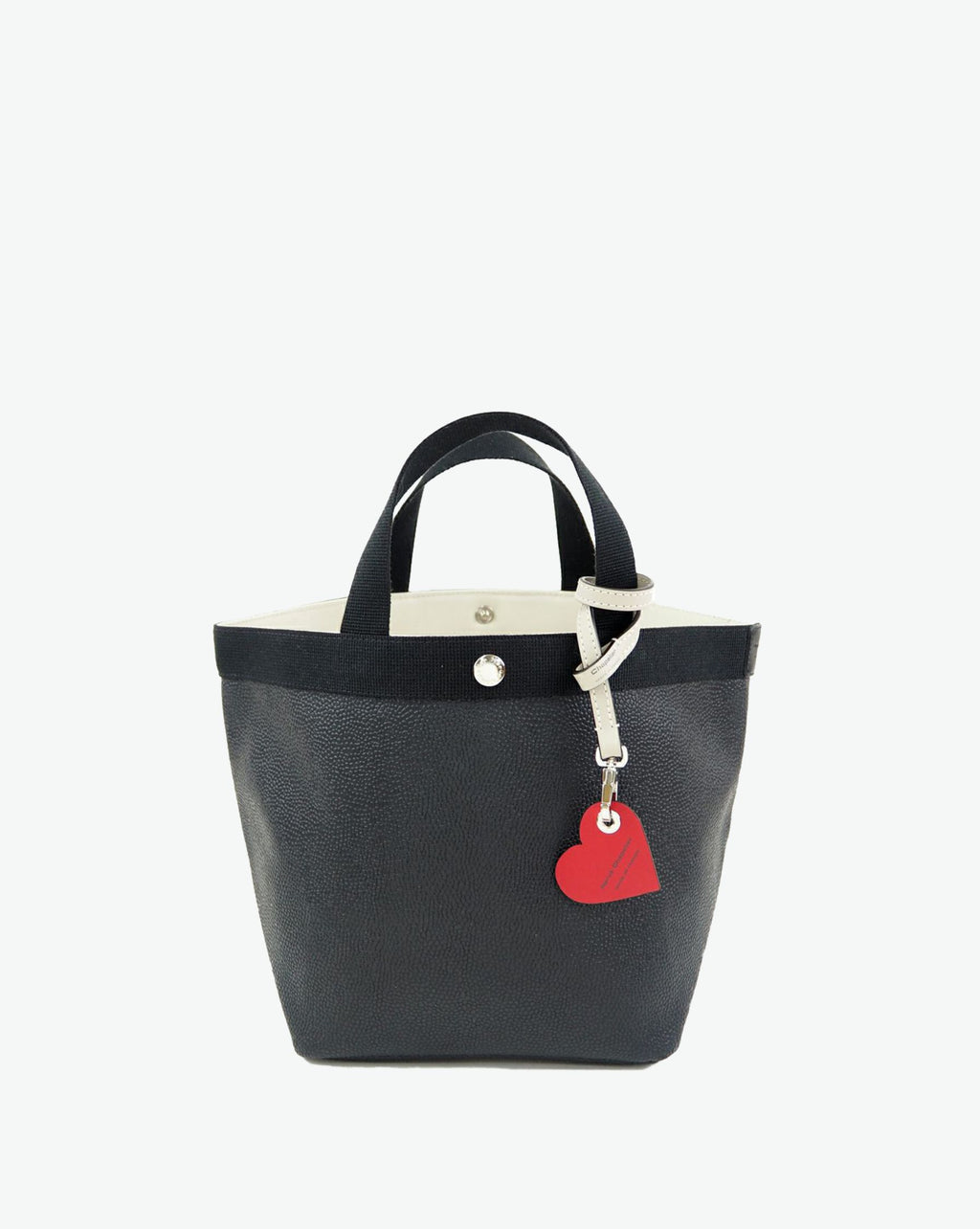 Packshot of a 122L flat charm in the shape of a heart with the Hervé Chapelier logo. The charm is made of leather with a eyelet in the middle in a XXS size. Charme en forme de coeur en cuir dans une taille XXS