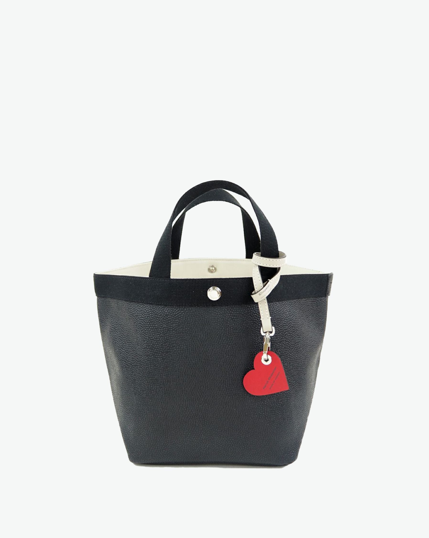 Packshot of a 122L flat charm in the shape of a heart with the Hervé Chapelier logo. The charm is made of leather with a eyelet in the middle in a XXS size. Charme en forme de coeur en cuir dans une taille XXS
