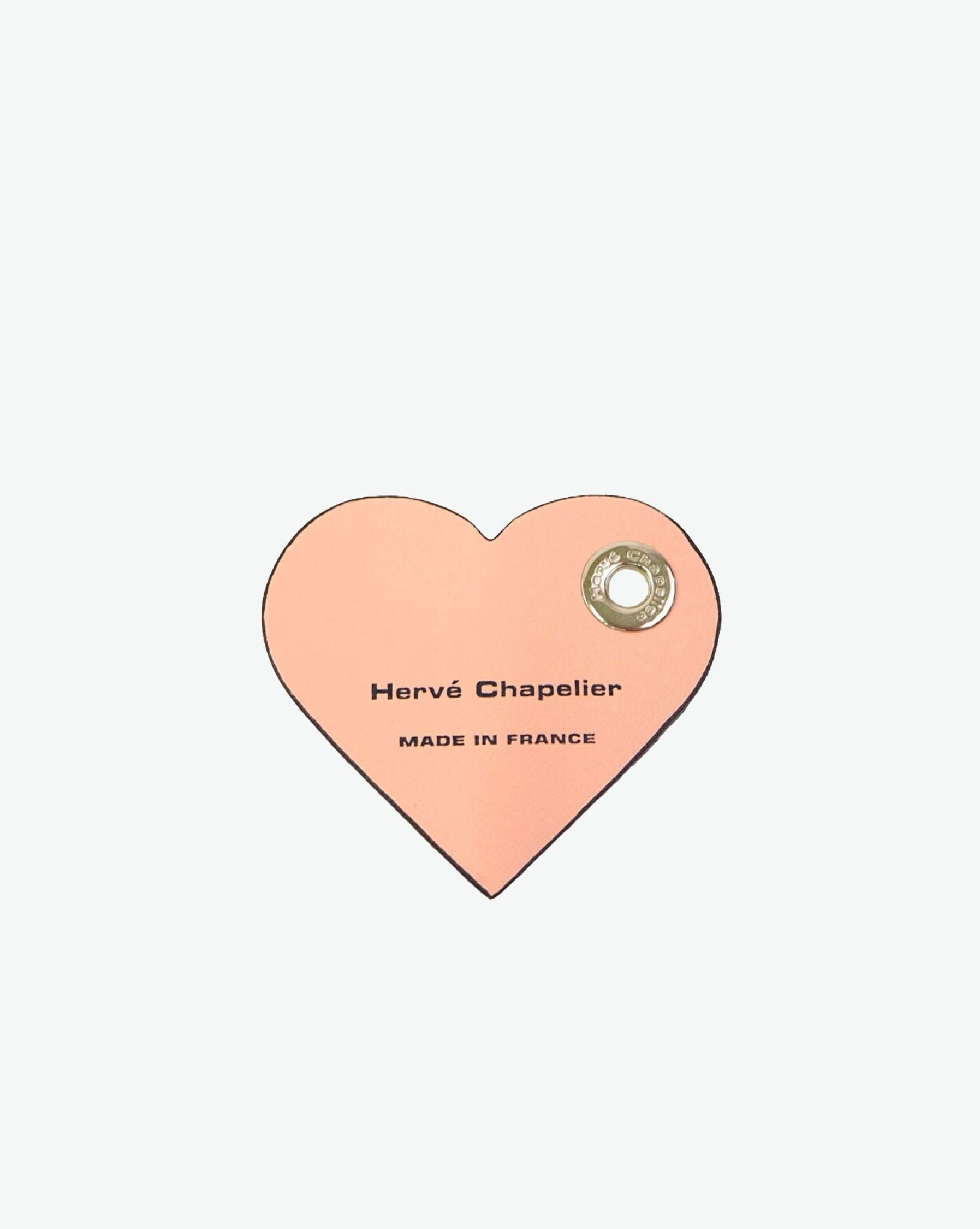 Packshot of a 122L flat charm in the shape of a heart with the Hervé Chapelier logo. The charm is made of leather with a eyelet in the middle in a XXS size. Charme en forme de coeur en cuir dans une taille XXS