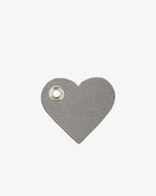 Packshot of a 122L flat charm in the shape of a heart with the Hervé Chapelier logo. The charm is made of leather with a eyelet in the middle in a XXS size. Charme en forme de coeur en cuir dans une taille XXS
