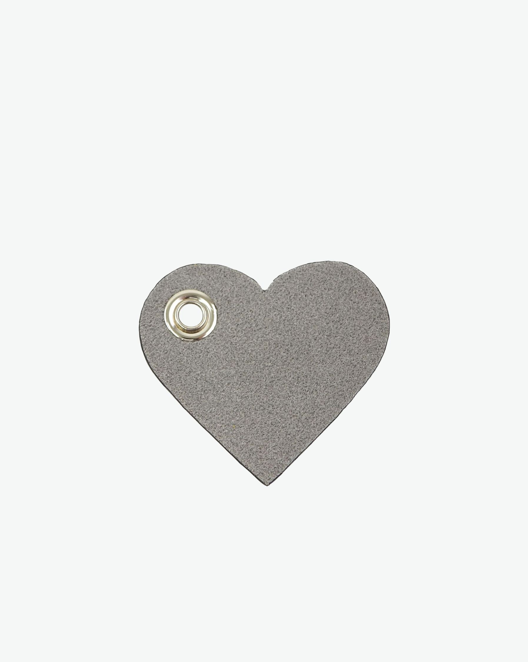 Packshot of a 122L flat charm in the shape of a heart with the Hervé Chapelier logo. The charm is made of leather with a eyelet in the middle in a XXS size. Charme en forme de coeur en cuir dans une taille XXS