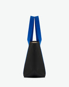 Sac porté épaule en toile enduite grainée, à fond rectangulaire et dans une taille M, et aux poignées longues de couleur à l'aspect coton faisant le tour du sac.