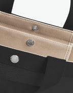 Sac à main en toile enduite grainée en taille M, au fond carré et aux poignées courtes de couleur à l'aspect coton, ainsi qu'à la poche intérieure avec bouton pression.