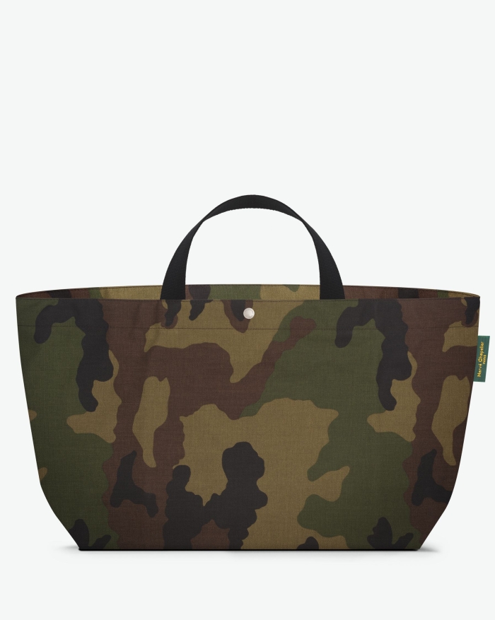 Visual on a white background of a large tote bag standing upright and straight, with short polycotton handles, a zipper and an inside pocket. The bag is made from printed polyamide fabric in a camouflage forêt noir motif. The Hervé Chapelier label is affi