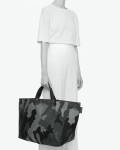 Visual of a standing woman holding a large tote bag through its short polycotton handles. The label is affixed on the right side with the Hervé Chapelier brand logo. This visual illustrates the 1838W bag by Hervé Chapelier.